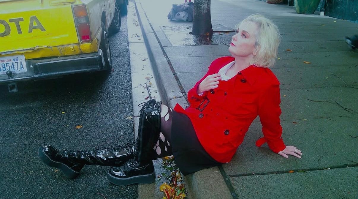 Woman in red coat sitting on street, yellow truck in background